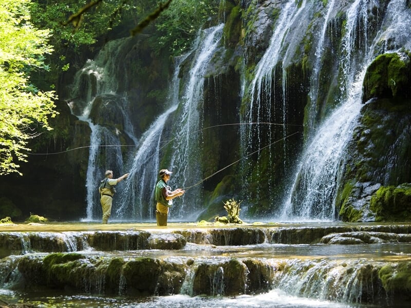 Deux pêcheurs à la mouche face à une cascade dans une belle rivière