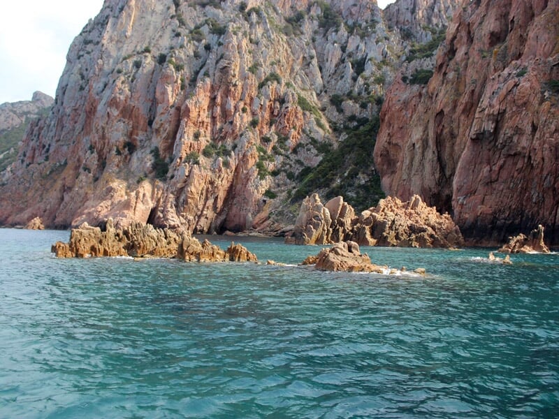 Rochers escarpés et formations rocheuses au bord d'une mer turquoise claire sous un ciel partiellement nuageux.