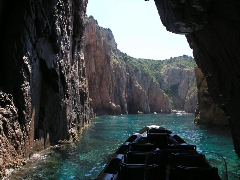 Vue depuis un bateau dans une crique étroite entourée de hautes falaises rocheuses et d'eau transparente.