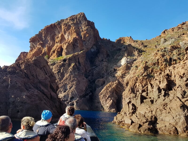 Groupe de personnes à bord d'un bateau pneumatique naviguant entre des falaises rocheuses rouges.