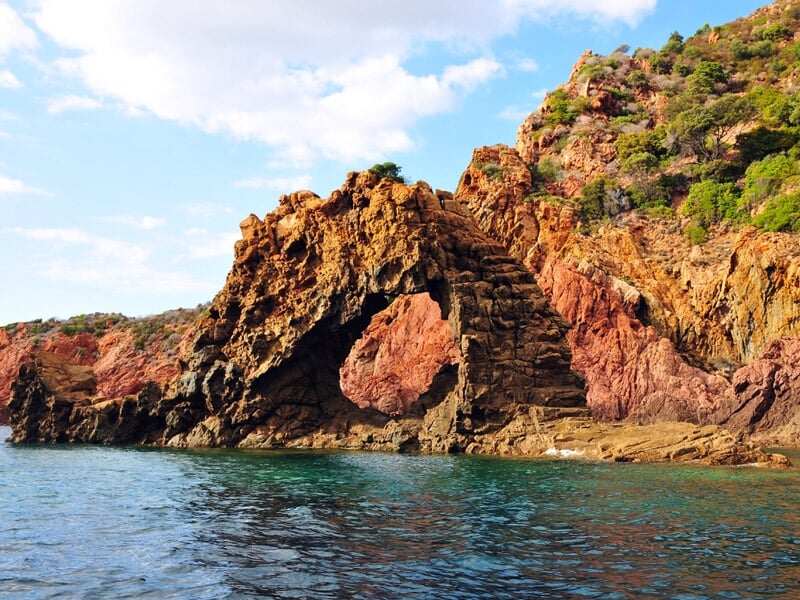 Arche naturelle formée par des rochers rouges au bord d'une mer turquoise claire sous un ciel ensoleillé.