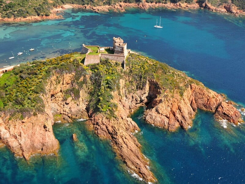 Vue aérienne d'une petite île rocheuse avec une tour ancienne entourée d'eau turquoise et de végétation verte.