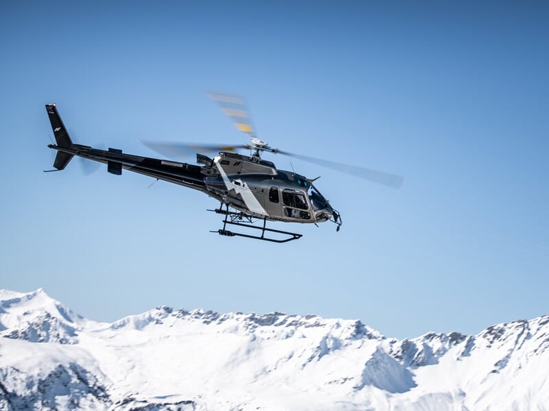 Hélicoptère en vol au-dessus de montagnes enneigées sous un ciel bleu clair sans nuages.