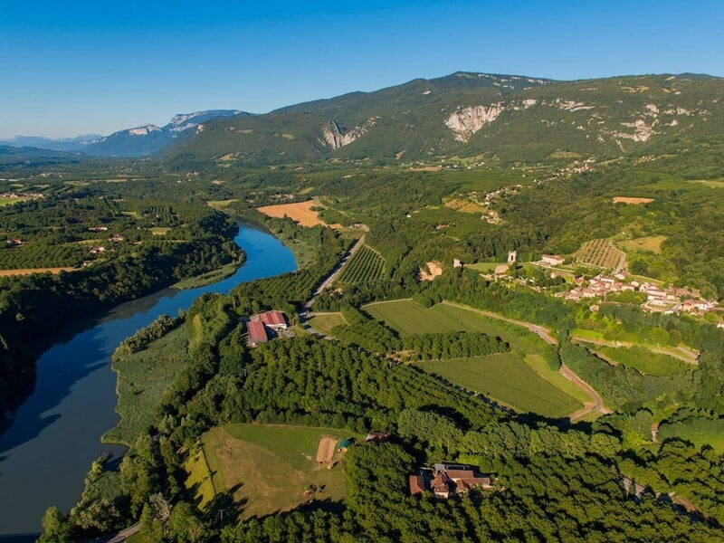 Vue aérienne d'une vallée verdoyante avec une rivière sinueuse, des champs cultivés et des collines boisées.