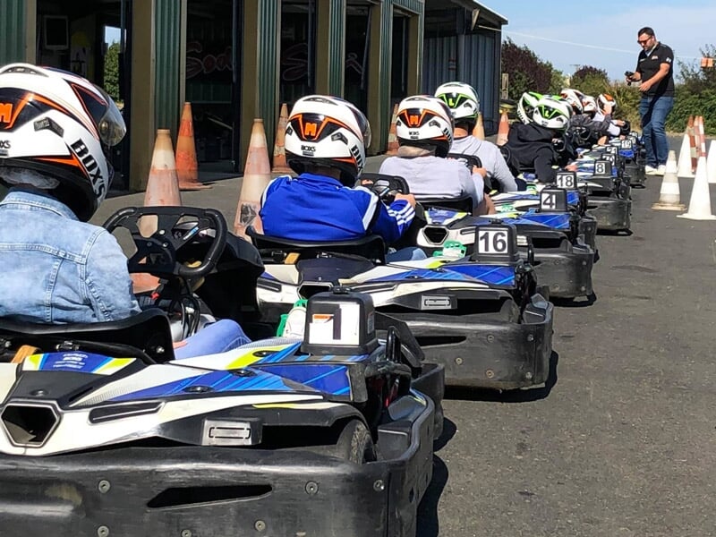 Groupe de personnes portant des casques blancs assises dans des kartings alignés sur une piste extérieure.