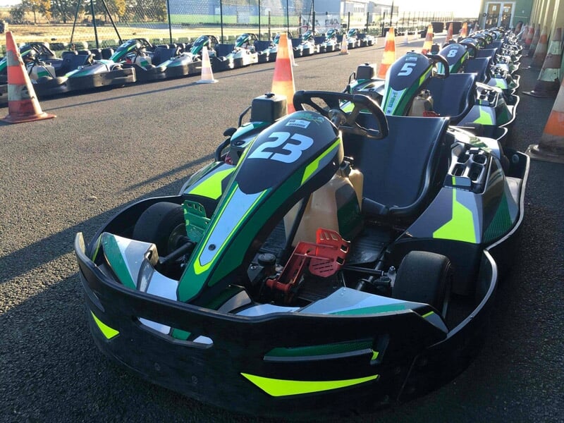 Karting noir et vert avec le numéro 23 garé sur une piste extérieure sous un ciel ensoleillé.