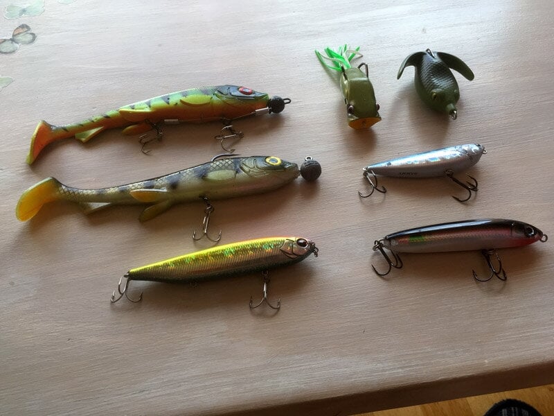 Plusieurs leurres de pêche colorés sont disposés sur une surface en bois, prêts à être utilisés pour la pêche.