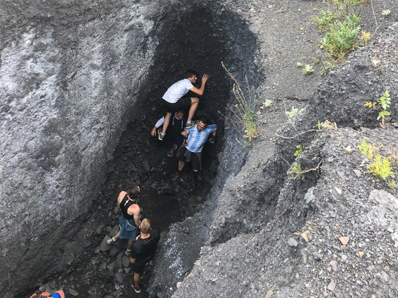 Groupe de personnes explorant une crevasse étroite dans un terrain rocheux et accidenté.