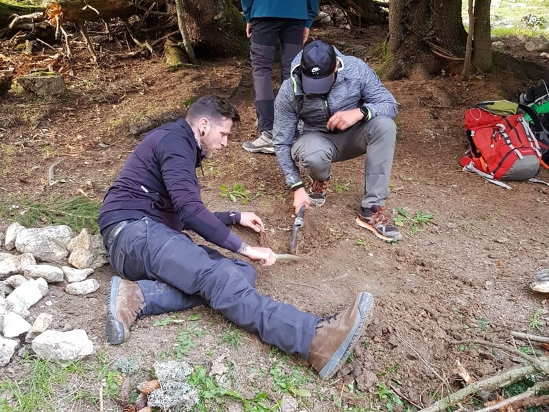 Deux hommes allumant un feu en frottant des bâtons dans un campement en forêt.