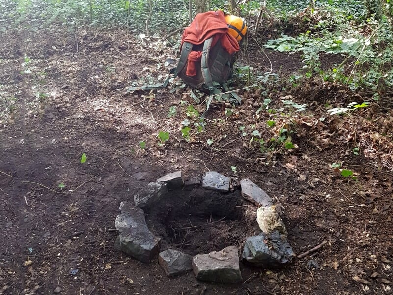 Cercle de pierres formant un foyer vide dans une zone boisée, prêt pour un feu de camp.
