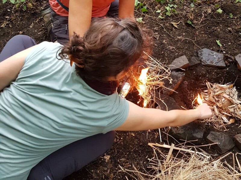 Personne allumant un feu de camp en utilisant des brindilles sèches dans un environnement forestier.