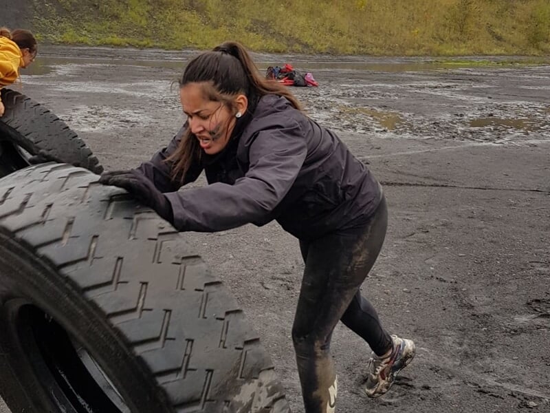 Femme poussant un gros pneu dans un terrain boueux, concentrée sur son effort physique.