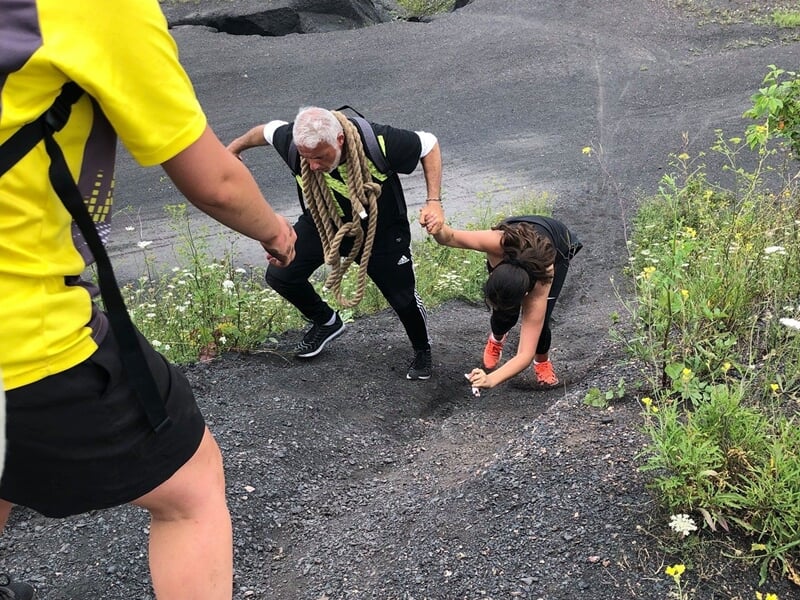 Personnes aidant un homme à grimper une pente raide et rocheuse en pleine nature.
