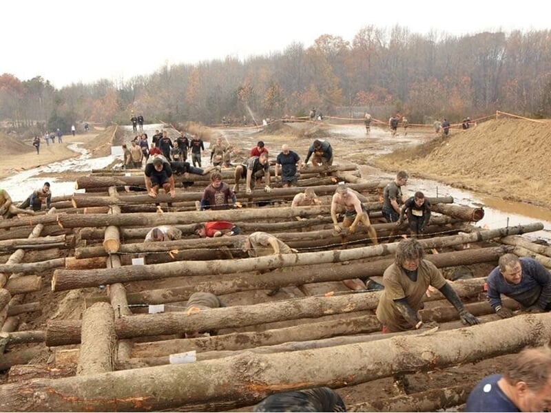 Groupe de personnes franchissant un obstacle en bois lors d'une course d'endurance en plein air.