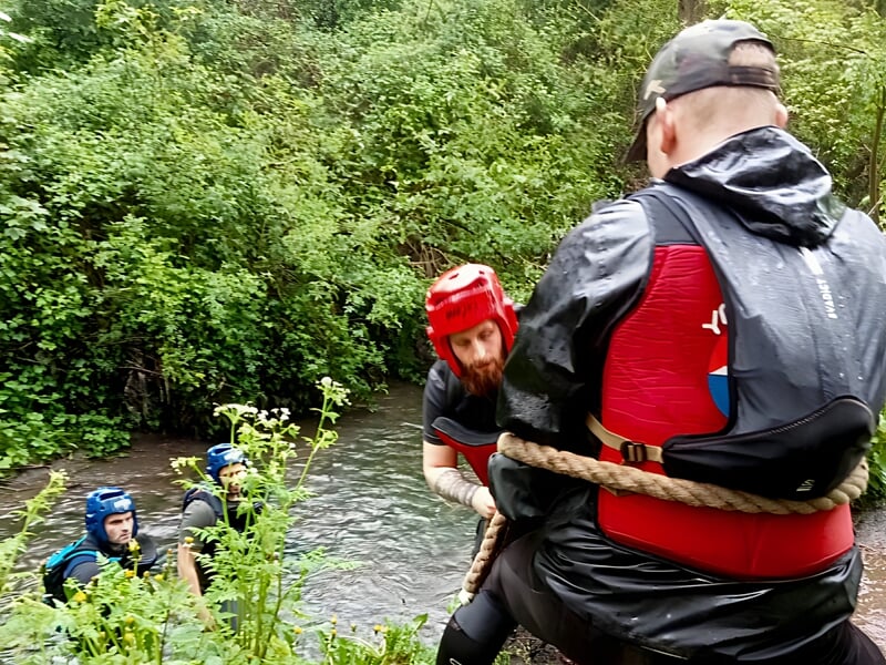 Quatre hommes en tenue de protection participent à un stage commando près d'une rivière en forêt dense.