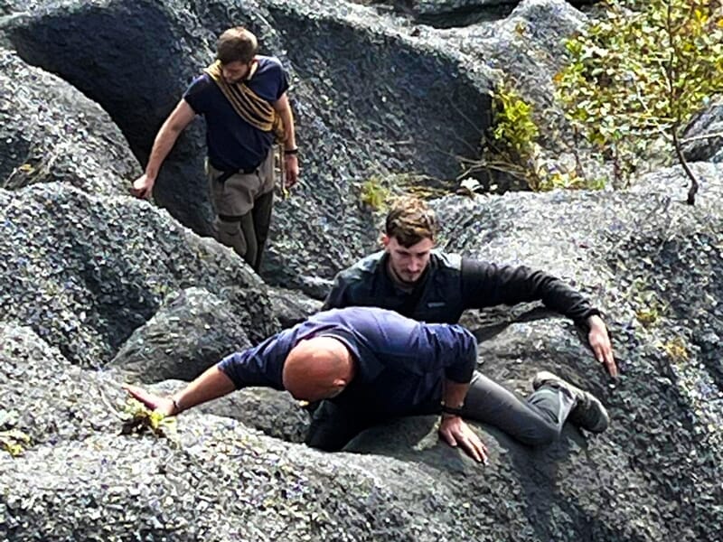 Trois hommes escaladent des rochers escarpés dans un environnement naturel pendant un stage commando à Hénin-Beaumont.