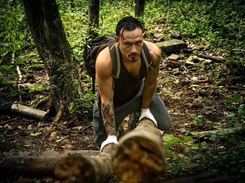 Un homme concentré soulève un tronc d'arbre dans une forêt dense pendant un entraînement physique commando.