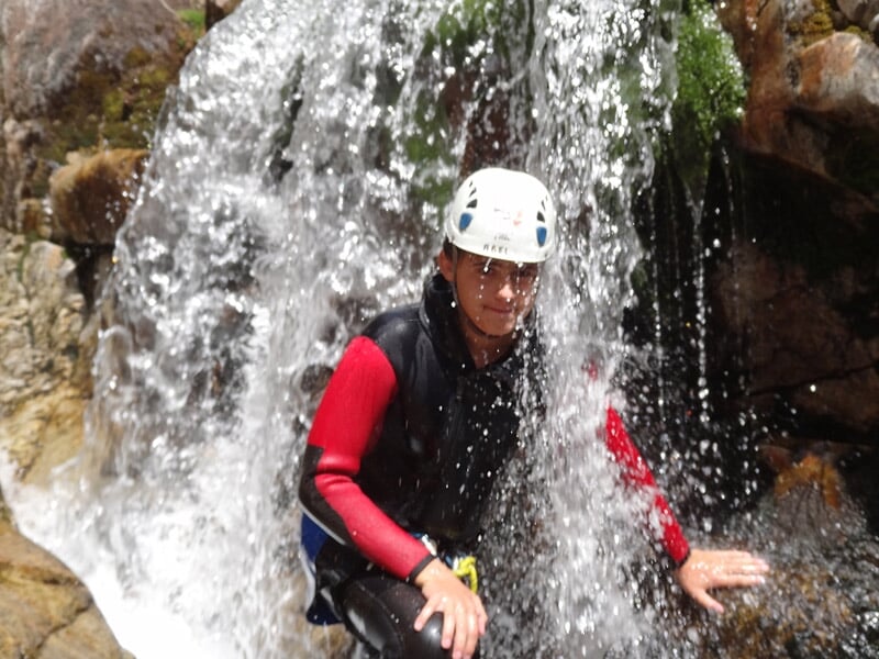 Personne en tenue de canyoning sous une cascade d'eau claire dans un environnement rocheux naturel.