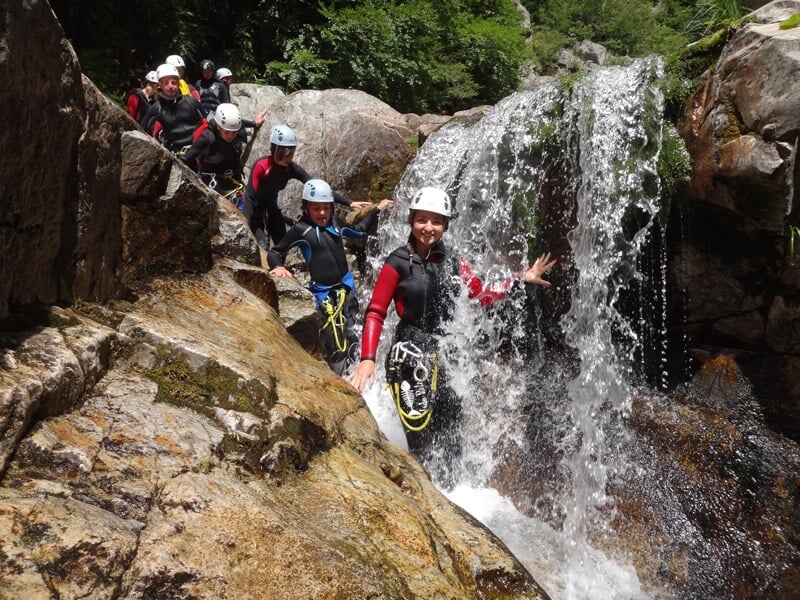 Groupe de personnes en équipement de canyoning descendant une cascade rocheuse entourée de végétation verte.