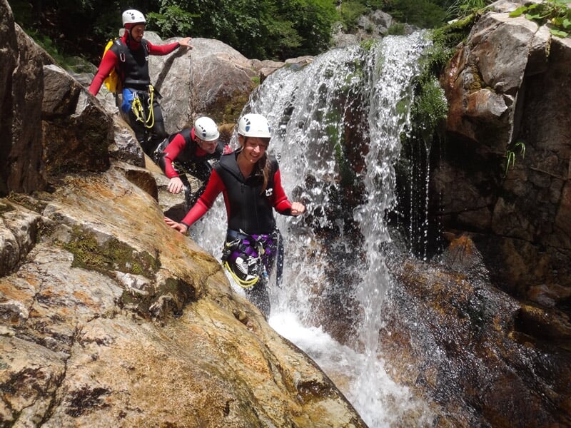 Participants au canyoning progressant le long d'une cascade avec des casques et combinaisons de protection.
