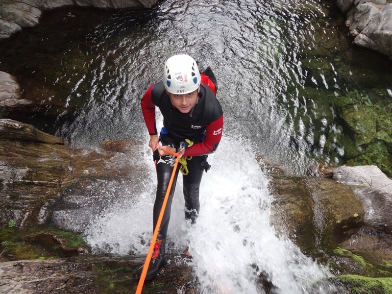 Personne en rappel sur une corde descendant une cascade d'eau vive dans un canyon rocheux.