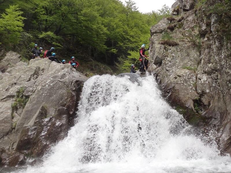 Vue d'une cascade puissante dans un canyon avec plusieurs personnes en tenue de canyoning en arrière-plan.