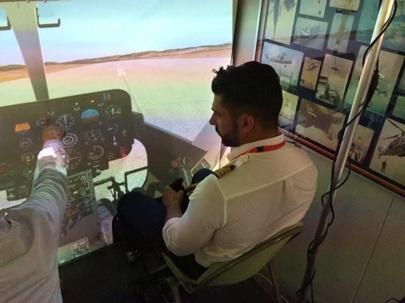 Deux hommes dans un simulateur de vol, l'un montre les commandes à l'autre dans un environnement d'entraînement.