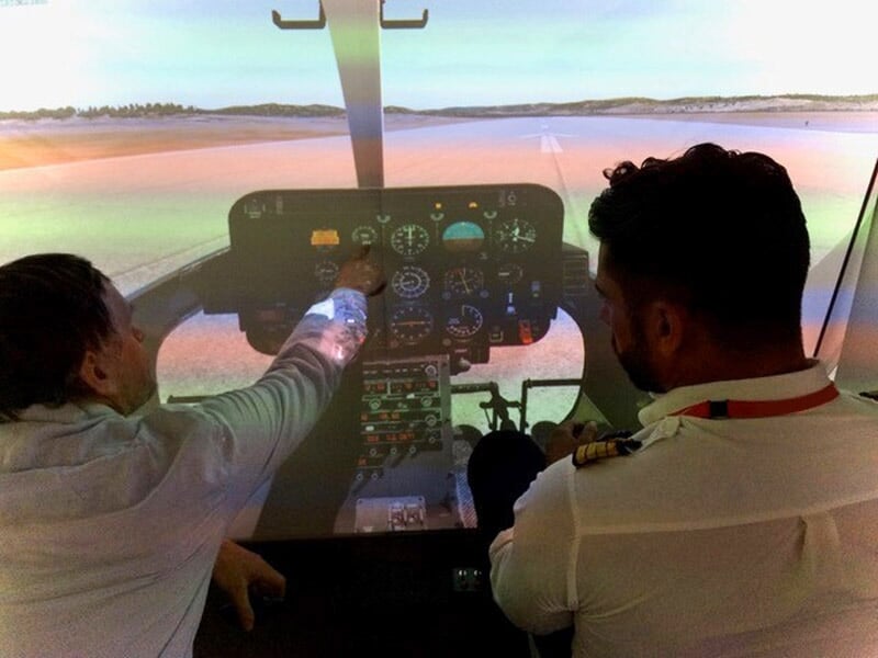 Deux hommes dans un simulateur de vol, l'un explique les instruments de bord à l'autre dans une salle d'entraînement.