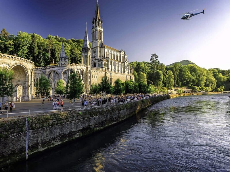 Vue d'un hélicoptère volant au-dessus d'une rivière près d'une grande église gothique entourée d'arbres verts.