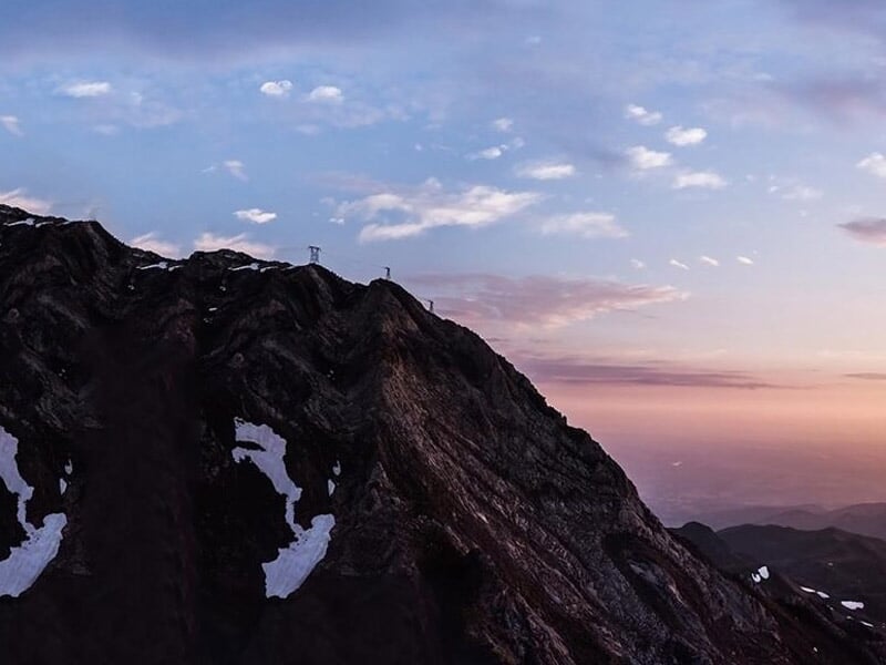 Paysage de montagne avec des sommets rocheux partiellement enneigés sous un ciel aux couleurs du coucher de soleil.