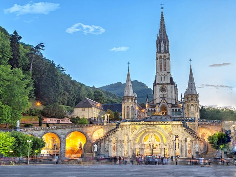 Église illuminée au crépuscule avec des arches en pierre et des collines boisées en arrière-plan.