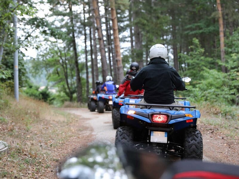 Groupe de personnes en quad bleu roulant sur un chemin forestier entouré d'arbres verts.