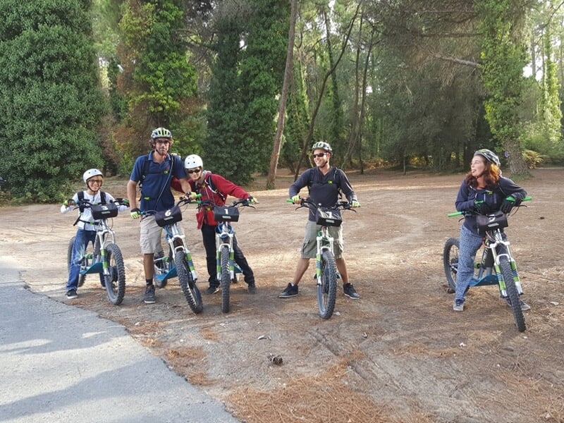 Groupe de cinq personnes avec leurs vélos électriques posant sur un chemin forestier entouré d'arbres verts.