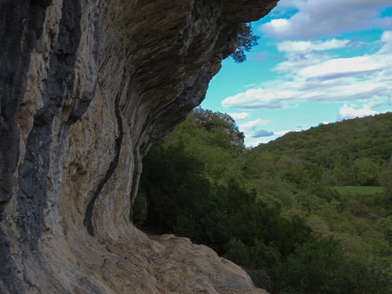 Paroi rocheuse courbée de la grotte avec vue sur la forêt et un ciel bleu avec nuages.