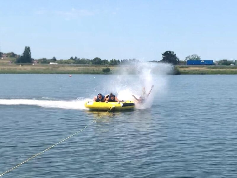 Chute d'une personne tombant d'une bouée tractée jaune sur un lac calme sous un ciel bleu.