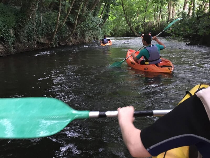 Deux personnes pagayant en kayak orange sur une rivière entourée d'arbres verts.