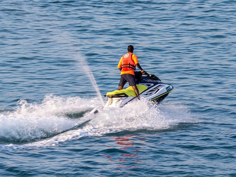 Homme debout conduisant un jetski jaune sur un lac, créant un sillage d'eau.