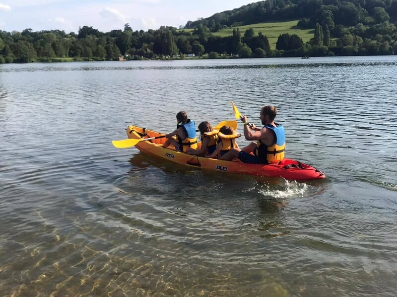 Quatre personnes pagayant ensemble dans un grand kayak rouge sur un lac entouré de collines.
