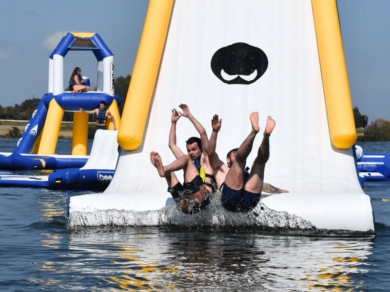 Groupe de personnes glissant ensemble d'une grande glissade aquatique sur un parcours d'obstacles, exprimant l'excitation et l'amusement pendant leur descente