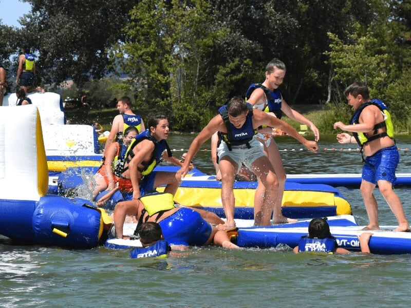 Personne effectuant un handstand sur un parcours d'obstacles gonflable, démontrant agilité et équilibre, avec d'autres participants marchant ou observant autour