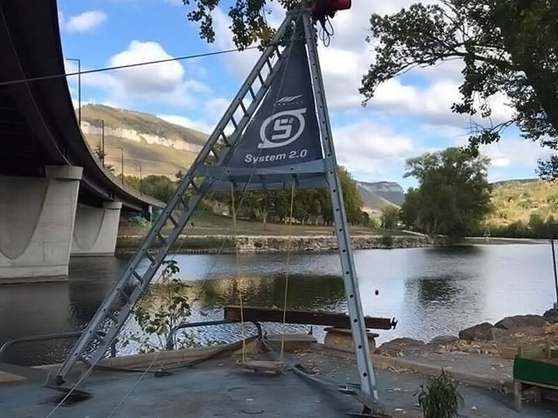 Structure métallique installée au bord d'une rivière sous un pont, avec paysage naturel en arrière-plan.