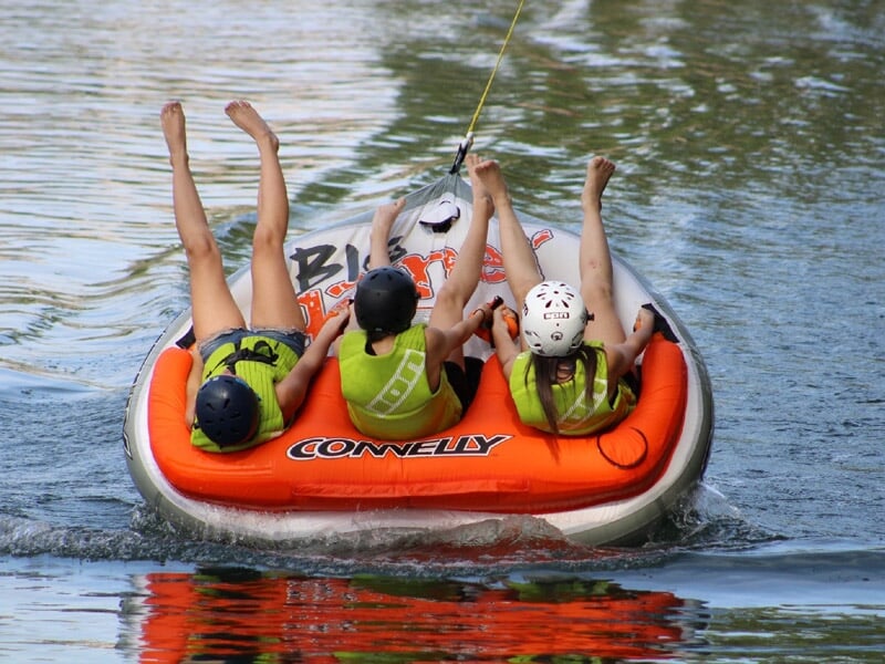 Trois personnes en gilets de sauvetage sur une bouée tractée sur l'eau, jambes levées en l'air.