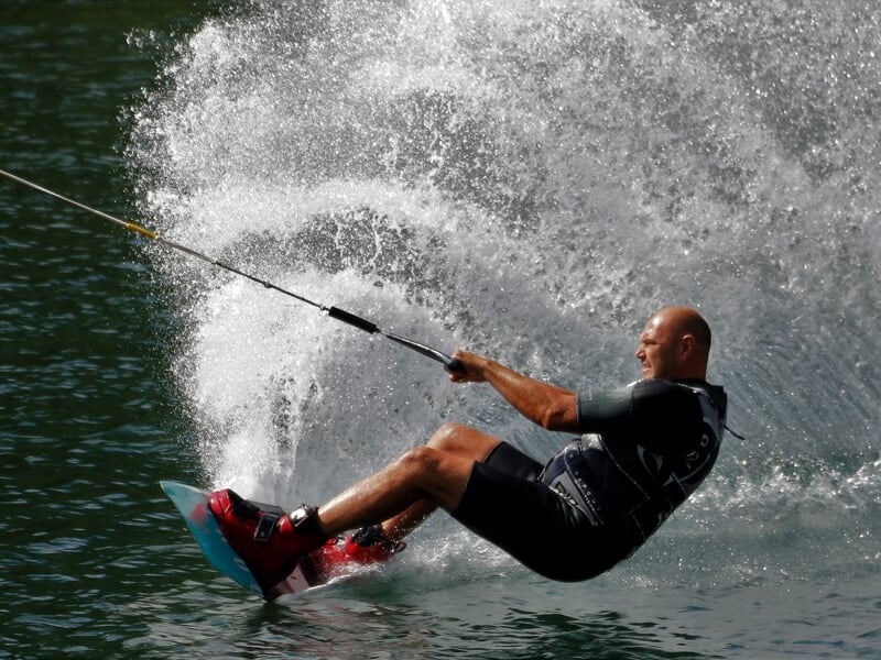Homme en wakeboard tiré par un câble, penché en arrière avec une grande éclaboussure d'eau.