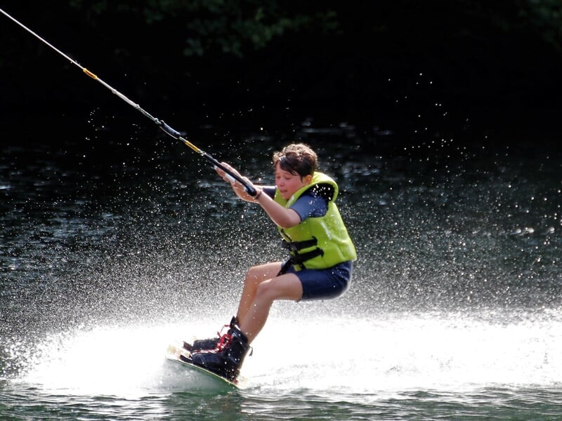 Jeune garçon en wakeboard tiré par un câble, glissant sur l'eau avec éclaboussures.