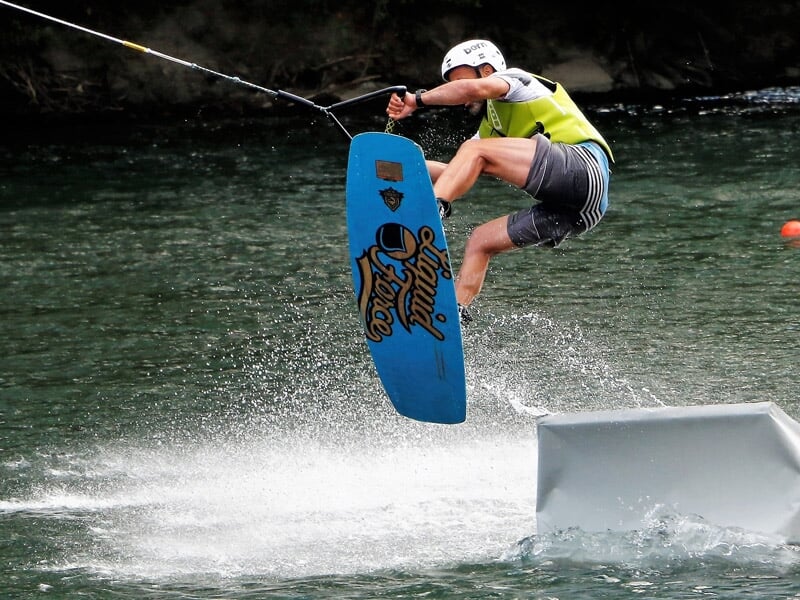 Jeune garçon en wakeboard avec casque et gilet, effectuant un saut avec la planche en l'air.