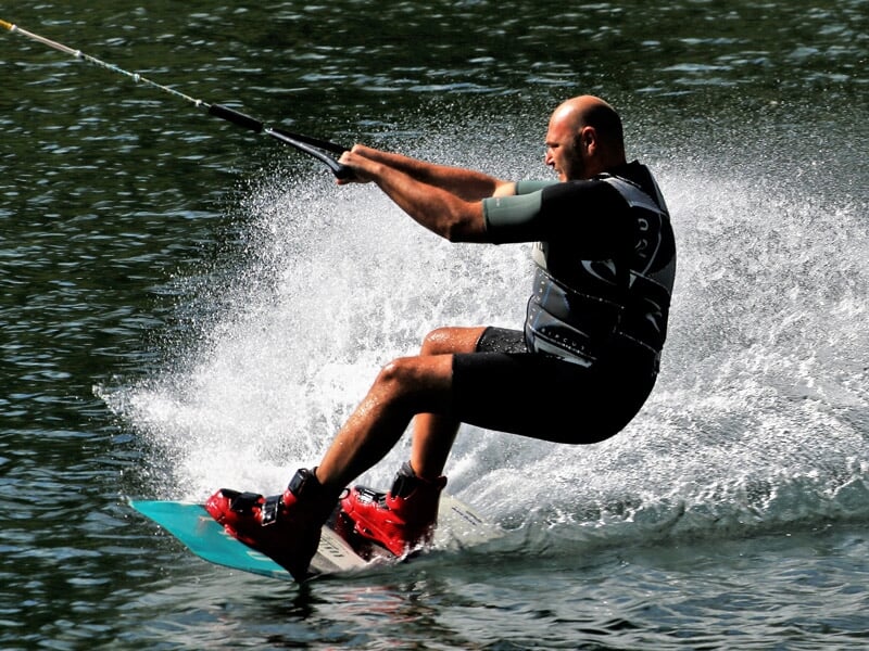 Homme en wakeboard tiré par un câble, glissant rapidement sur l'eau avec éclaboussures.
