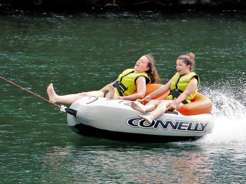 Deux filles en bouée tractée sur l'eau, portant des gilets de sauvetage jaunes.