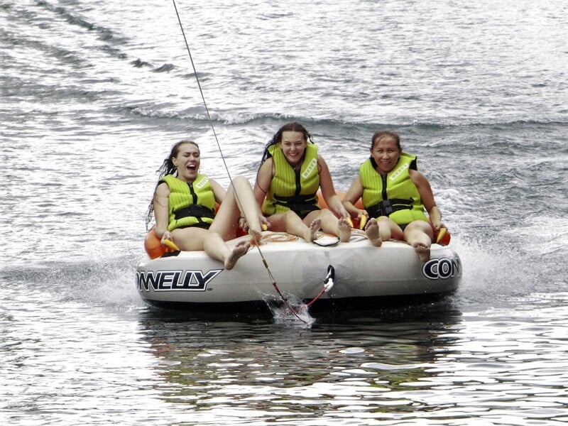 Trois filles assises sur une bouée tractée sur l'eau, toutes portant des gilets de sauvetage.