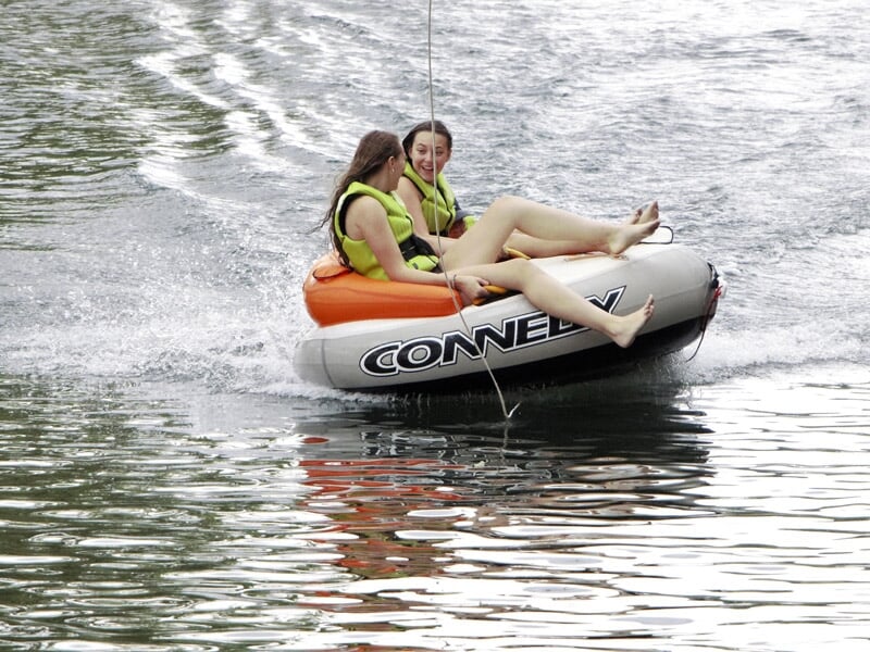 Deux filles assises sur une bouée tractée sur l'eau, souriantes et portant des gilets de sauvetage.