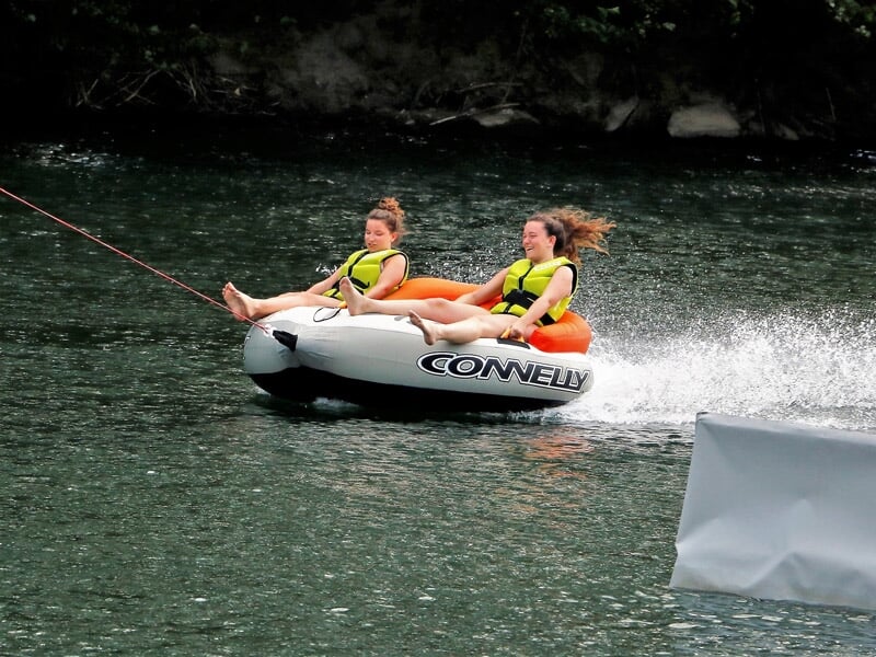 Deux filles en bouée tractée sur l'eau, souriantes et portant des gilets de sauvetage jaunes.